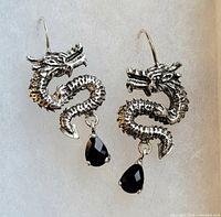 Pair of sterling silver dragon-shaped earrings with black teardrop gemstones against white background.