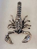 Front view of sterling silver scorpion pendant showing detailed sculpting and fleur-de-lis symbol on back.