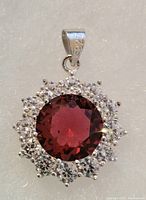 Front view showing the round ruby center surrounded by white topaz stones set in sterling silver with 925 mark on the bail.