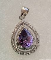 Front view of sterling silver pendant showing central pear-shaped amethyst surrounded by two rows of white topaz stones.