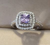 Front view of sterling silver ring showing square-cut amethyst center surrounded by double halo of white topaz stones and white topaz-studded band.