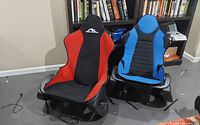 Front view of two gaming chairs side-by-side with red/black and blue/black upholstery and seat covers partially detached