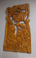 First wood carving panel showing two seated humans with a dog under trees and a hut, carved in relief on wood.