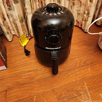 Front view of the Elite Gourmet black air fryer showing the pull handle and control dials on a wooden floor.