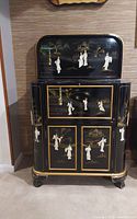 Full front view of closed cabinet showing lacquer finish, painted gold accents, and mother-of-pearl geisha figures