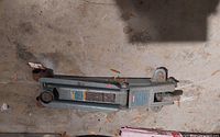 Hydraulic floor car jack lying on the concrete floor, showing the jack's body, handle, and wheels.