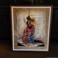Full view of the framed art print showing the entire artwork with the kneeling figure in colorful clothing.