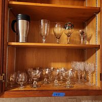 Wide view of shelf showing assortment of stemmed and stemless vintage glassware including champagne coupes, wine glasses, and a travel mug.
