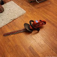 Full view of the Craftsman 20-inch electric hedge clippers lying on wooden floor, showing the orange and black body and the long metal blade.
