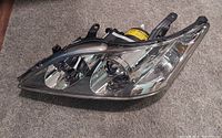 Left front headlight assembly for Lexus ES 350 placed on carpeted floor showing multiple reflective bulbs and black mounting brackets.