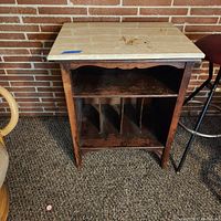 Front view of the solid wood magazine cabinet with vertical dividers and an open shelf beneath a marble top, showing wear consistent with use.