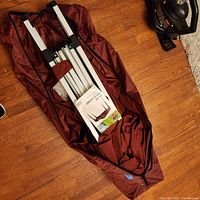 Portable pop-up gazebo folded inside rust-colored carry bag on hardwood floor, showing partial frame inside.
