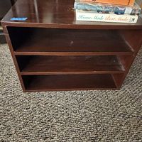 Front view of the wooden short bookcase showing three horizontal shelves with some books on top.