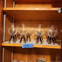 Set of 6 water glasses with clear bowls and dark smoked crystal thick cone-shaped stems on a wooden shelf.