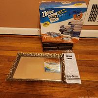 Box of Ziploc Space Bags, vanity mirror with ornate gold frame, and a tissue packet on the floor.