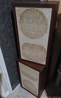 Two rectangular wooden cabinet speakers with fabric grills, showing circular and oval impressions from speaker drivers.