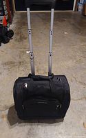 Front view showing black rolling travel bag with extended telescoping handles and two wheels at base