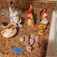 Photo with two ceramic roosters, one ceramic hen, ceramic sad clown figurine, ceramic Davar cocktail cherries Pixieware bowl, and ten pink rose ceramic place setting stands.