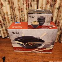 Photo showing boxed Parini 14-inch preseasoned wok set and boxed set of 4 ceramic rice bowls, with packaging and branding visible.