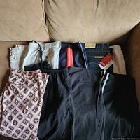 Set of eight pairs of women's casual pants laid out on couch in various colors and patterns, showing variety of styles and sizes.
