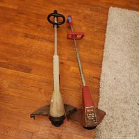 Two electric yard trimmers side by side on wooden floor, one white Craftsman and one red Toro