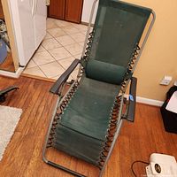 Front view of zero gravity lounger showing green mesh fabric seat and attached lumbar pillow with metal armrests and frame.