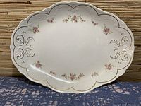 Full view of large white porcelain platter with pink floral designs and gold scalloped edge.