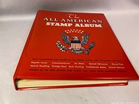 Red hardcover All American Stamp Album titled 'The All American Stamp Album' with a USA eagle crest on the front cover.