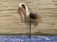 Side view of wooden crane figurine showing body paint and metal stand.