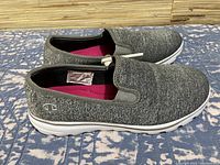 Side view of the women's Champion slip-on shoes showing gray fabric upper with Champion logo on the side and white sole.