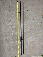 Full view of the two-piece fishing rod laid out beside a measuring tape indicating length of about 5 feet
