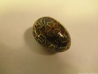 Top view of the small cloisonné egg showing floral enamel design with gold outlining on a dark background.