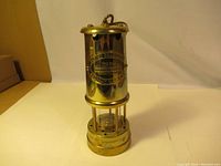 Full view of a vintage solid brass coal mining lamp with a cylindrical shape and glass enclosure, placed on a flat surface