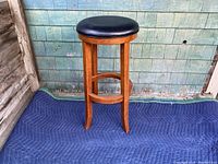 Front view of the vintage solid wood barstool with black vinyl padded seat, showing curved legs and stretcher bars.