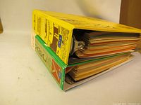 Side view of two vintage stamp collector albums stacked, showing thickness and metal fasteners.