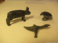 Three soapstone carvings displayed together: a dark quadruped animal, a bird perched on a base, and another bird with outstretched wings.