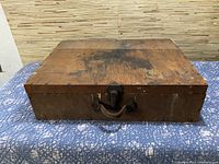 Top view of vintage wooden tool box showing wear and stains on the surface, with metal latch and handle visible on front edge.
