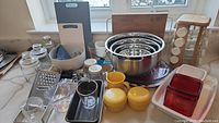 Overview of various kitchen bakeware and utensils on countertop showing jars, measuring cups, bowls, spice rack, and cutting boards.