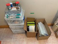Stack of plastic storage boxes and jars with beads on tiled floor
