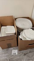 Two cardboard boxes containing white CorningWare dishes and platters, including oval and rectangular shapes.