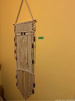 Macramé wall hanging made of cream rope with wood beads and fringed bottom, hanging on wall.