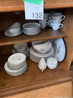 Photo showing full set of china dinnerware pieces arranged on wooden shelf, including plates, bowls, cups, cream and sugar pieces.