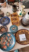Multiple decorative ceramic items on table including plates, bowls, serving dish, and vases mostly with floral designs.