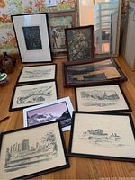 An overview photo showing 10 framed pictures on the floor, including sketches, cityscapes, boats, a floral painting, and a seascape.