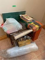 Overview of the lot showing plastic storage boxes, sewing machine case, yarn skeins, and large rolls of material on floor.