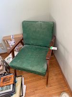 Full view of the MCM style single chair showing green patterned upholstery, wooden armrests, and wood legs with metal end caps. Visible wear on upholstery.