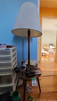 Full view of lamp showing pleated fabric shade, wooden post, tripod base with round side table, and overall condition