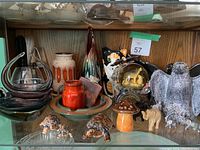 Wide shot of various decorative items including glass bowls, ceramic and pottery figures, and jars displayed on a wooden shelf.