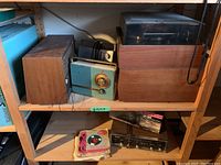 Top shelf items: wood-grain speaker, teal transistor radio, small camera, and wooden turntable with clear lid