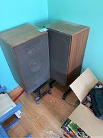 Pair of speakers on metal rolling stands against a teal wall, showing overall condition and placement